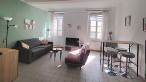 A living room with a sofa, a TV, a coffee table, and a dining area with stools.