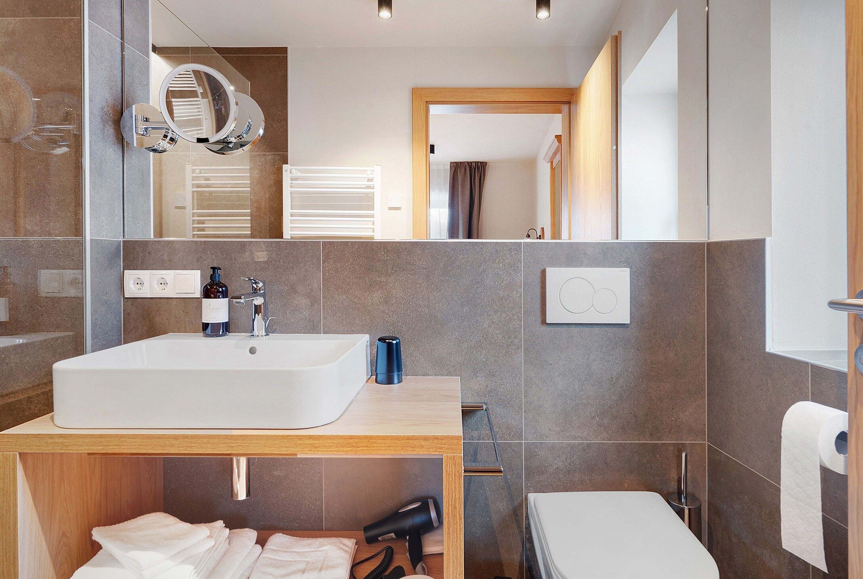 A modern bathroom with a large sink, mirror, towel rack, and toilet.
