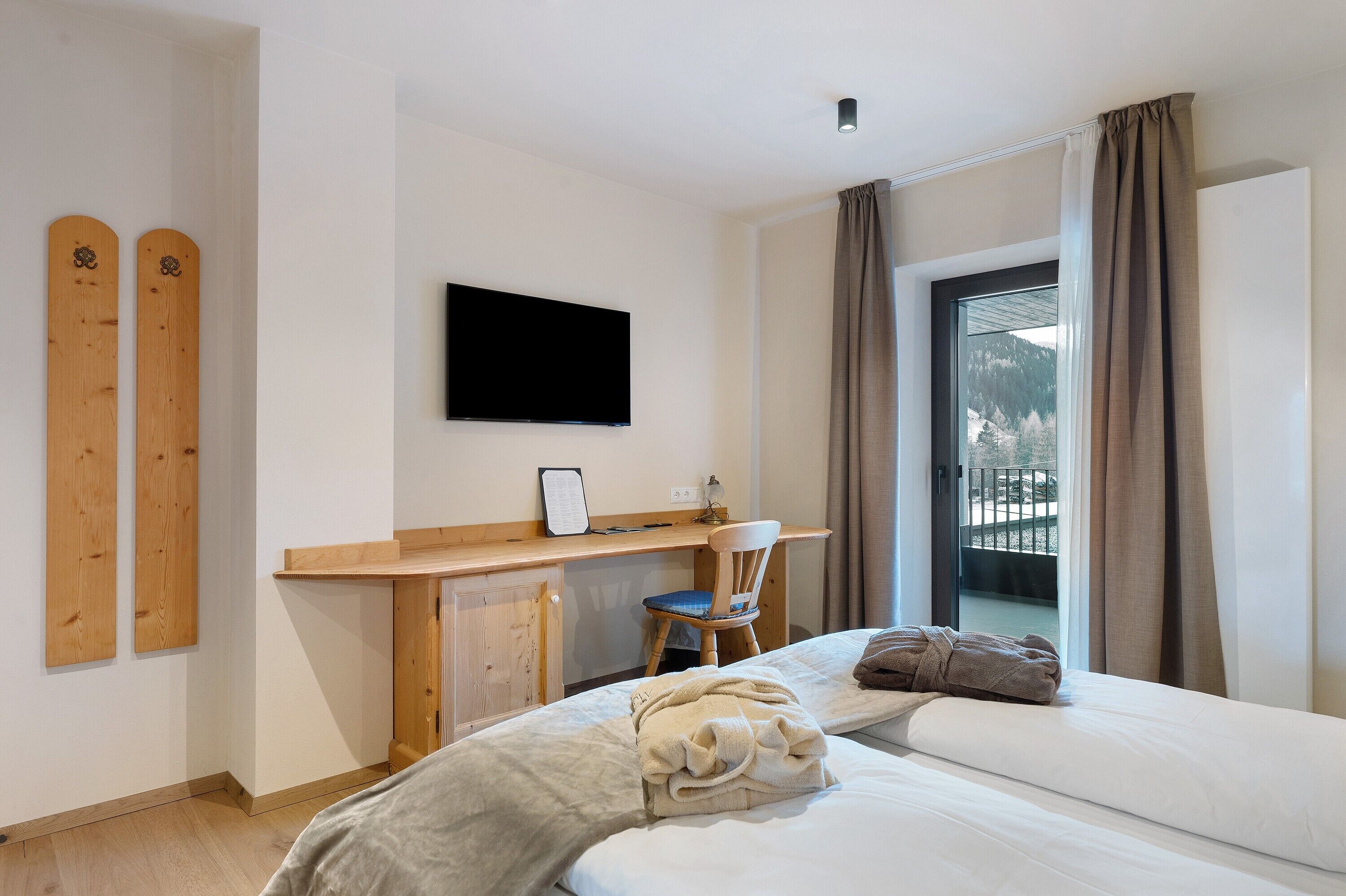 Une chambre d’hôtel équipée d’un lit, d’un bureau, d’une chaise, d’une télévision et offrant une vue sur les montagnes par la fenêtre.