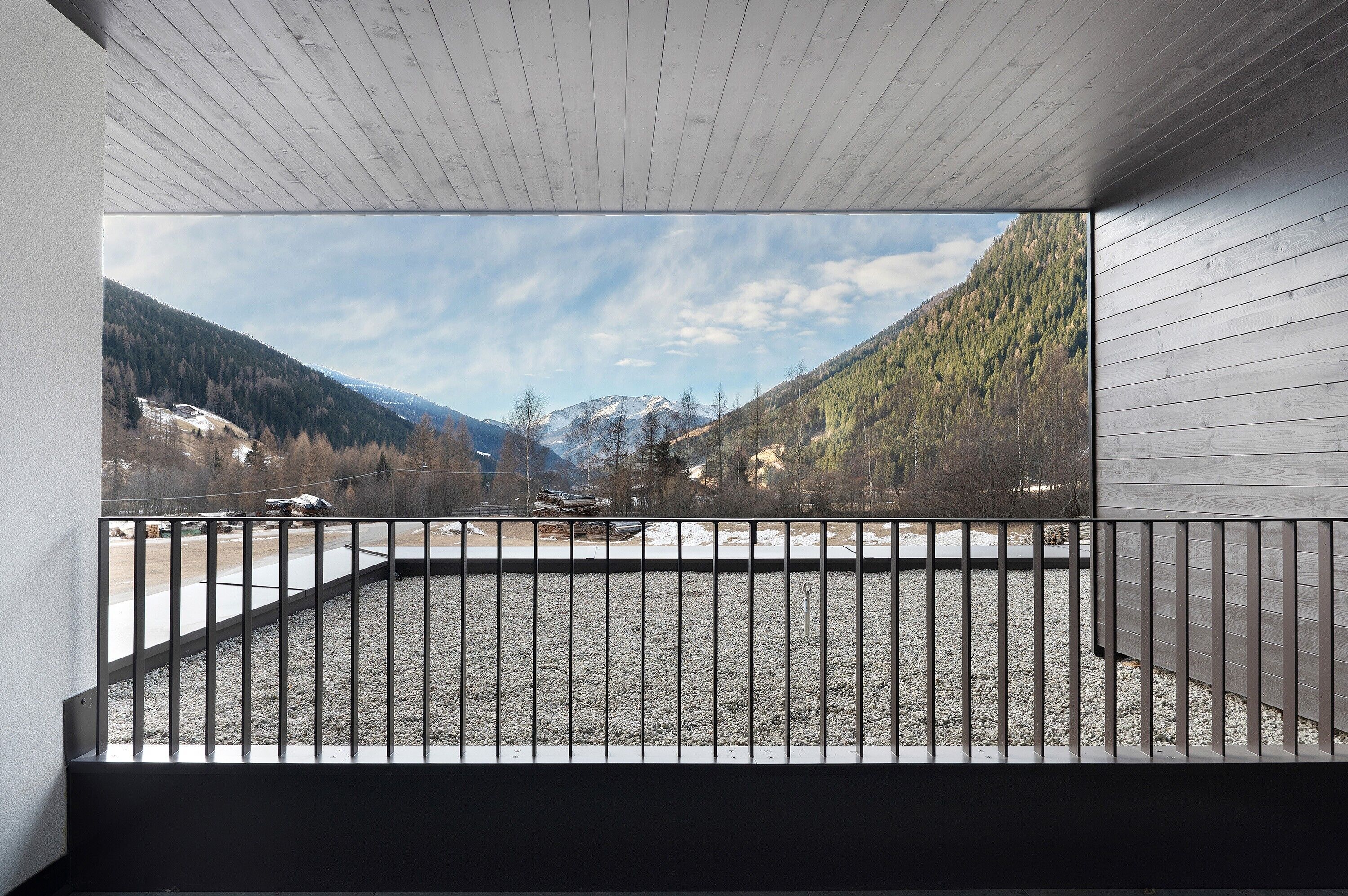 A balcony with a metal railing, a view of a mountainous landscape, and a wooden ceiling.