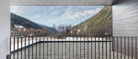 A balcony with a metal railing, a view of a mountainous landscape, and a wooden ceiling.