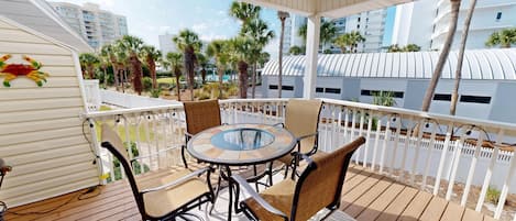 A covered outdoor area with a round glass table and wicker chairs, surrounded by a white fence and palm trees.