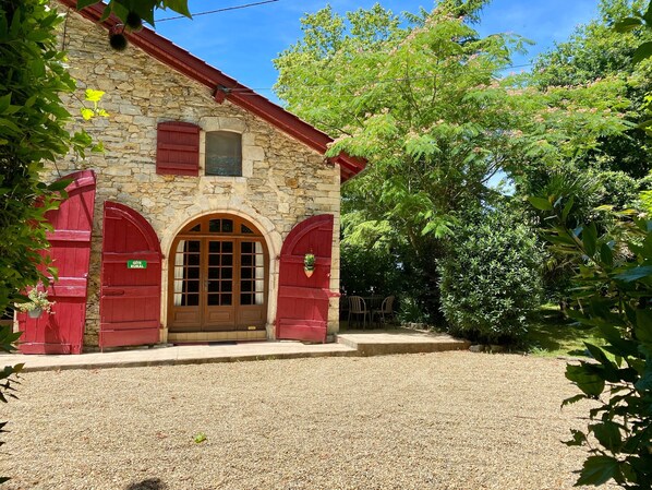 A stone building with a red door and arched windows, surrounded by greenery.