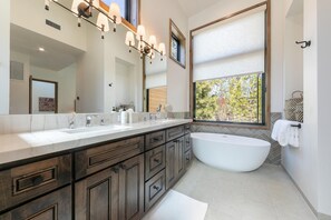 Ein modernes Badezimmer mit einem großzügigen Waschtisch, einer freistehenden Badewanne und einem großen Fenster mit Blick auf Bäume.