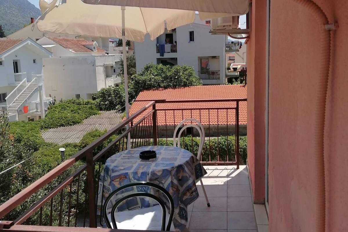 A balcony with a table and chairs, a white umbrella, and a view of neighboring buildings.