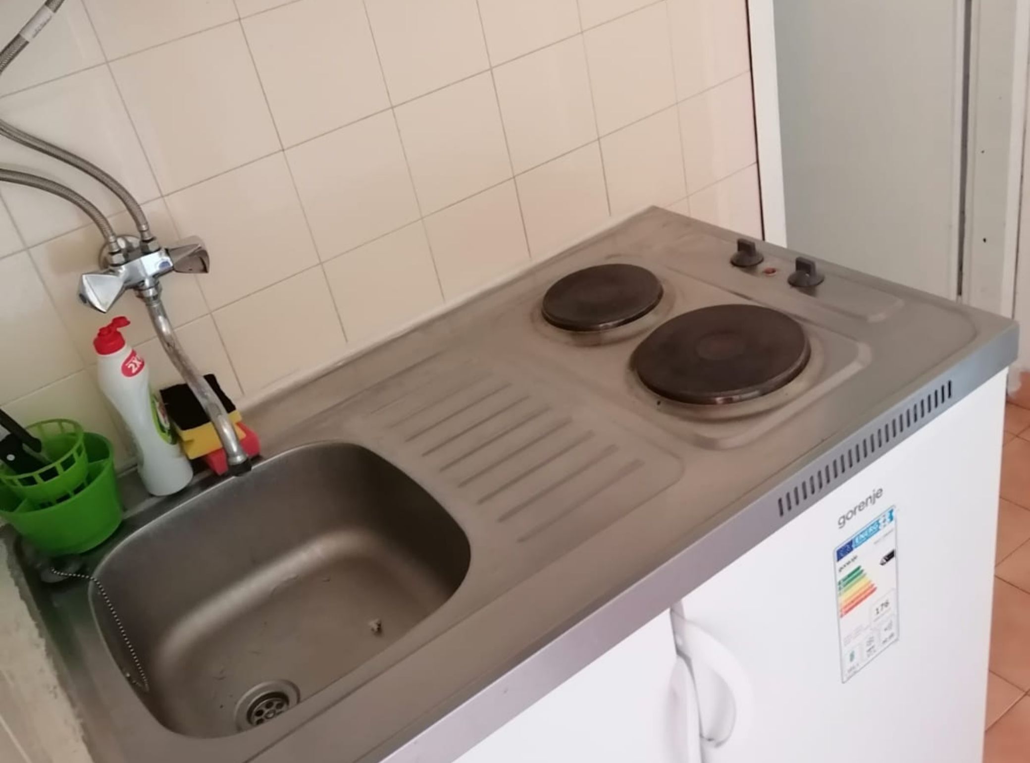 A compact kitchen with a sink, two stovetops, and a green basket.