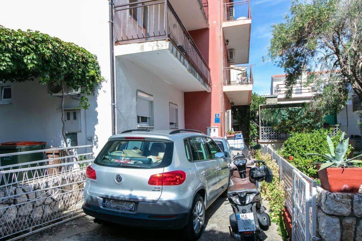 A silver car parked in front of a building with balconies and a motorcycle beside it.