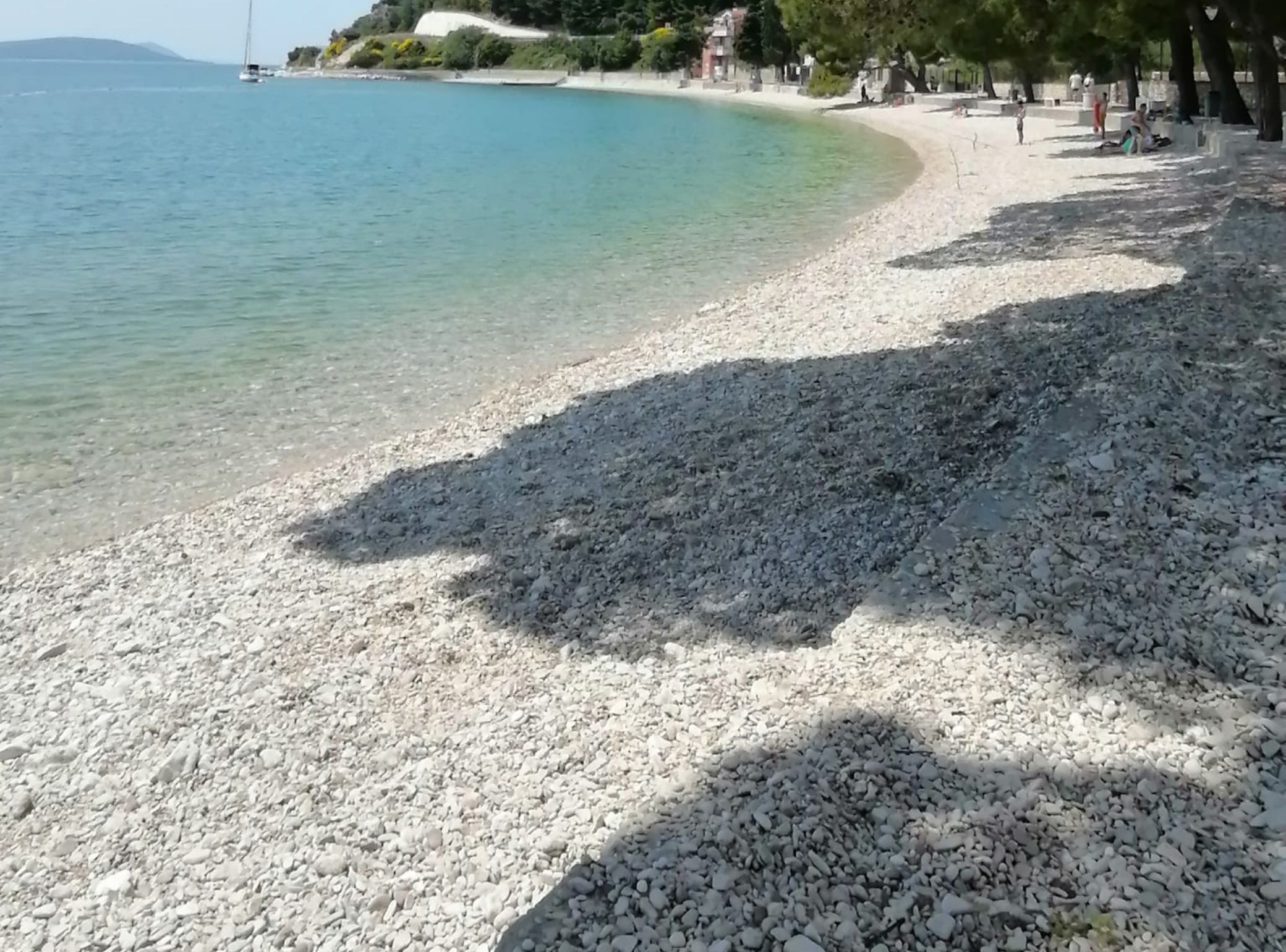 Una playa de guijarros con agua cristalina y algunas personas a lo lejos.
