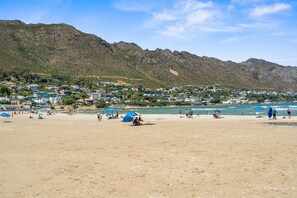 Una playa con casas al fondo y una cadena montañosa.