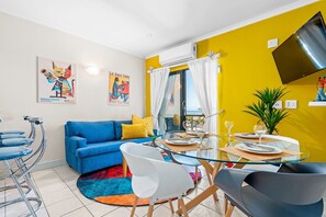 A modern living room with a blue sofa, a glass dining table, and a yellow accent wall. - Gordon's Village View (Cape Town)