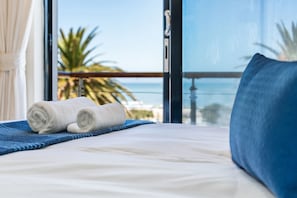 A bed with white linens, a blue pillow, and a rolled towel on a blue striped blanket. - Gordon's Village View (Cape Town)