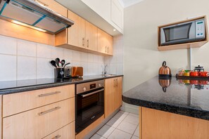 Una cocina moderna con armarios de madera, horno Bosch, microondas y cafetera.
