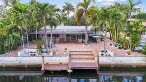A waterfront property with a dock, outdoor seating, and lush tropical vegetation. - Waterfront 4BR Retreat w/HotTub Dock & Outdoor Bar (Fort Lauderdale)