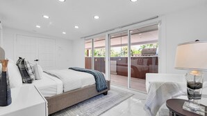 A modern bedroom with a bed, a nightstand, a lamp, and a view of an outdoor patio with a grill. - Waterfront 4BR Retreat w/HotTub Dock & Outdoor Bar (Fort Lauderdale)