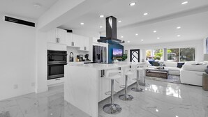 A modern kitchen with white cabinetry, a central island with bar stools, a built-in oven, and a stainless steel refrigerator. - Waterfront 4BR Retreat w/HotTub Dock & Outdoor Bar (Fort Lauderdale)