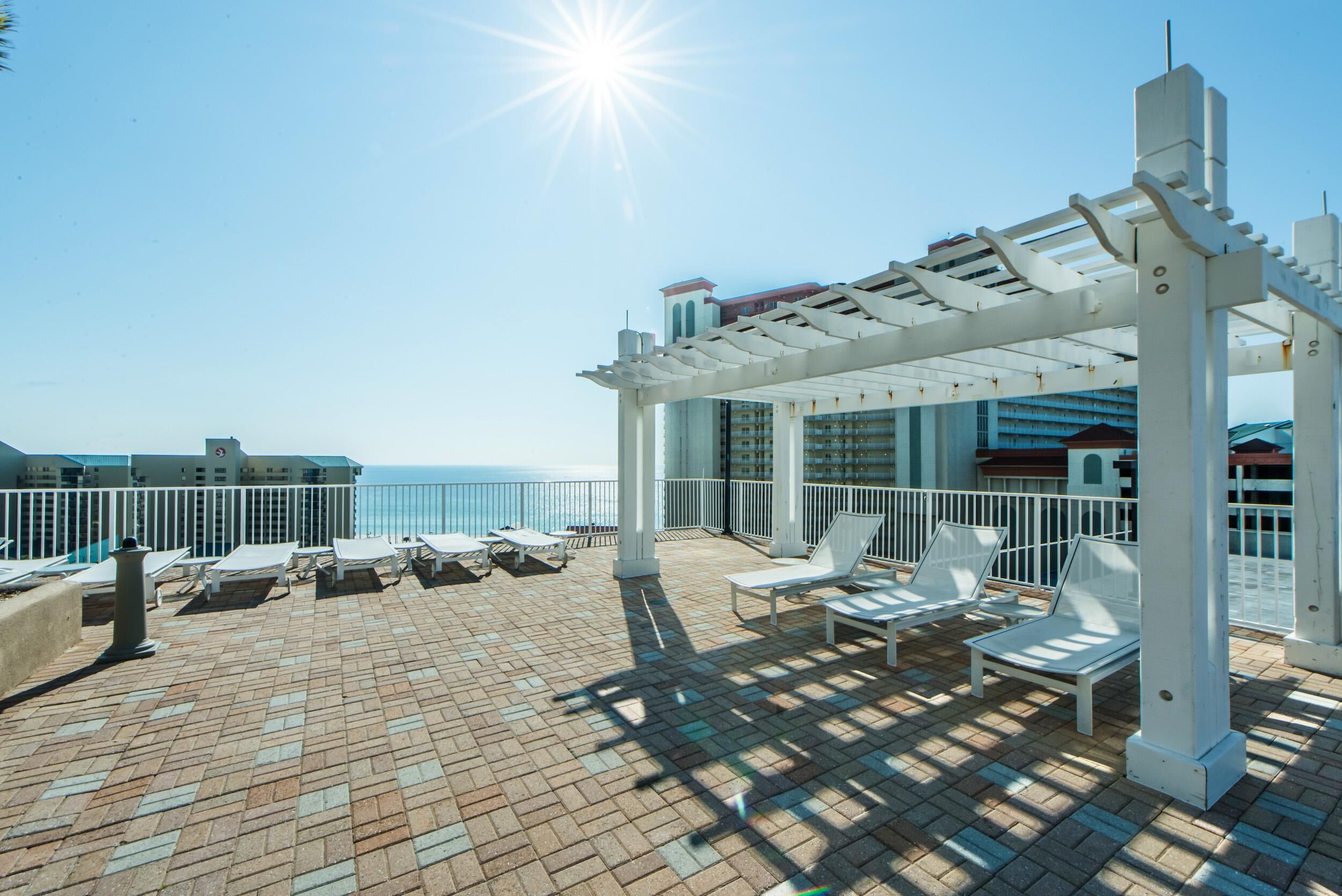A sunlit outdoor deck with white lounge chairs and a pergola, overlooking the sea.
