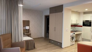 Habitación de hotel moderna con cama, escritorio, silla, armario, lavadora y kitchenette.