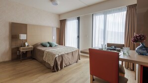 Una habitación de hotel con cama, mesita de noche, lámpara y un área de comedor con mesa y sillas.