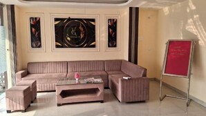 A modern living room with a sectional sofa, a glass coffee table, and a red information board. - HOTEL VIJAYA GRAND  (Patna)