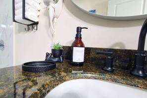 Une salle de bain avec un comptoir en marbre, un distributeur de savon liquide, une petite plante en pot et un porte-serviettes.