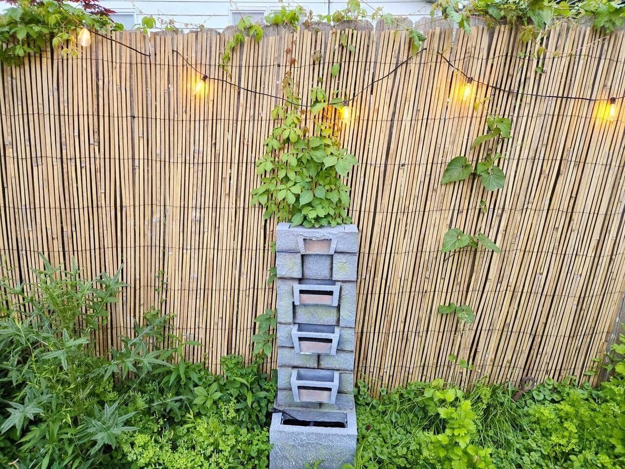 Un jardin agrémenté d’une clôture en bambou, d’un bac à fleurs en pierre et de guirlandes lumineuses.