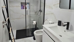 A modern bathroom with a glass-enclosed shower, a toilet, and a sink with a mirror above it. - K&K Apartments (Machico)