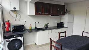 A compact kitchen with a washing machine, a microwave, a coffee maker, and a sink. - K&K Apartments (Machico)