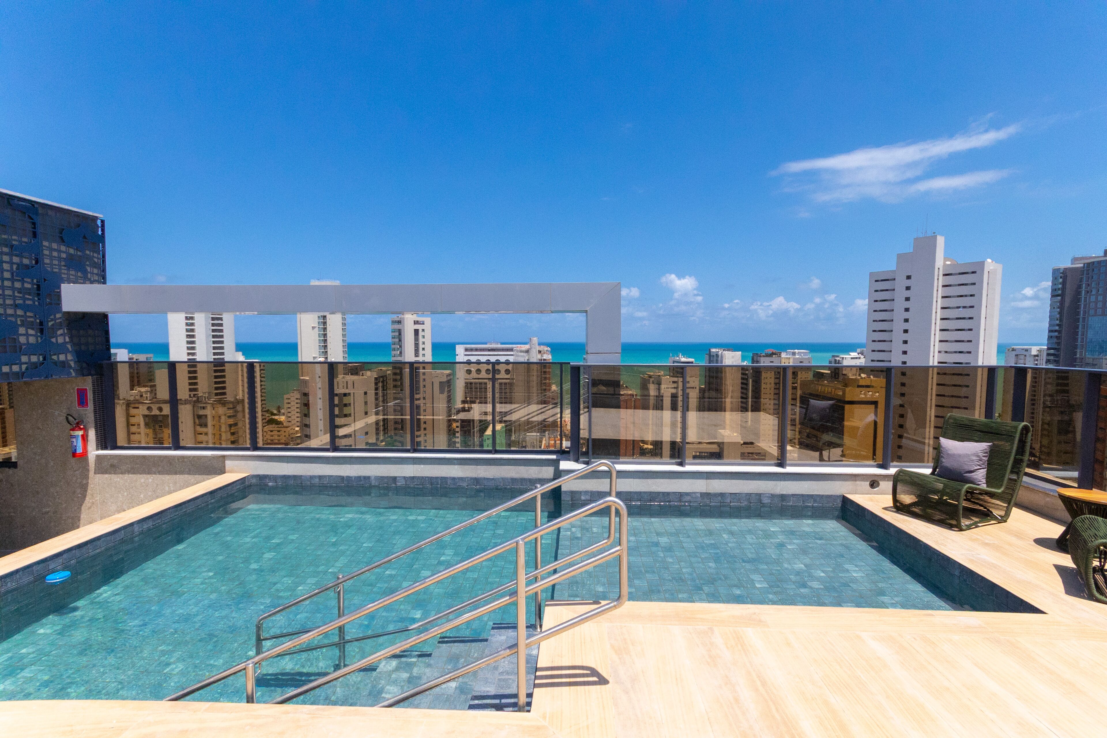 A rooftop swimming pool with a clear view of the ocean and city skyline.