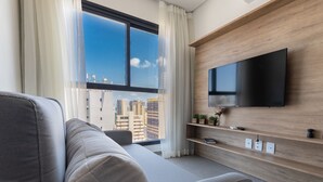 Ein modernes Wohnzimmer mit einer Couch, einem an einer Holzwand montierten Flachbildfernseher und Stadtblick durch große Fenster.