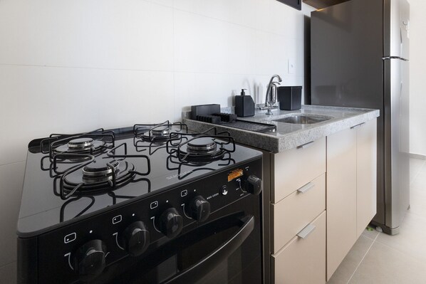 A kitchen with a gas stove, oven, sink, and a refrigerator. - Andrea Priori em Boa Viagem By Carpediem (Recife)