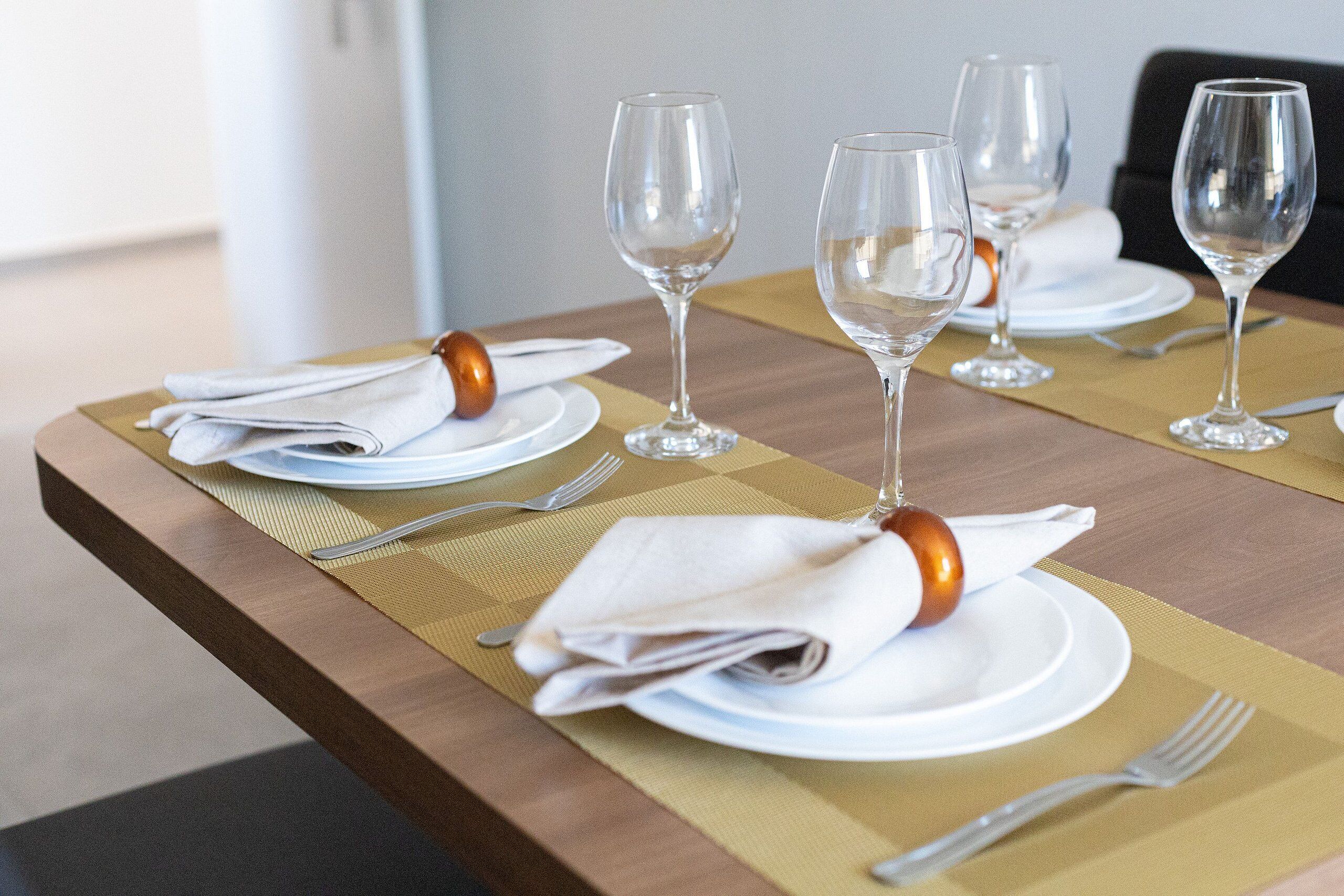 A dining table set with white plates, folded napkins, and clear wine glasses.