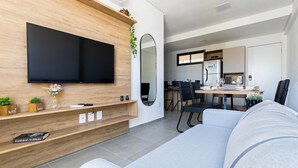 Ein modernes Wohnzimmer mit Flachbildfernseher, Holzregalen, einer Couch und einem Essbereich mit Stühlen und Tisch.