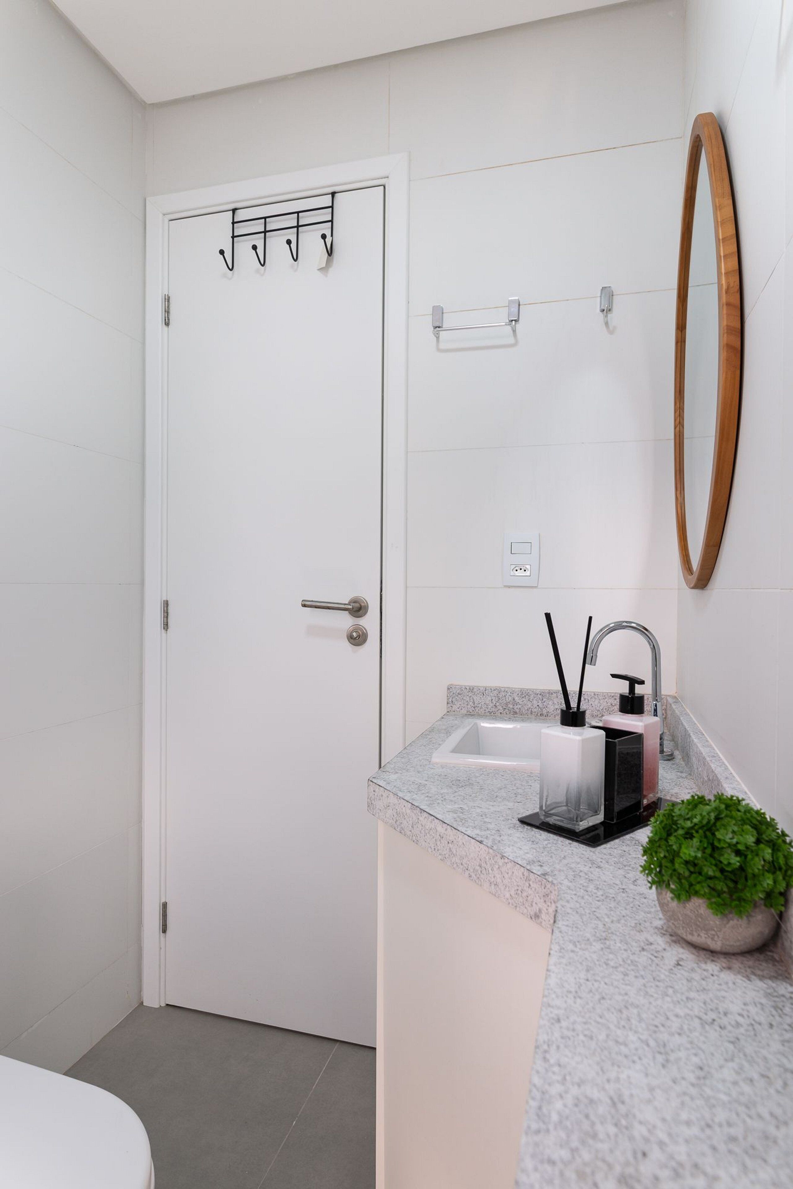 Une salle de bain avec une porte blanche, un lavabo doté d’un robinet moderne, un miroir et une petite plante en pot.