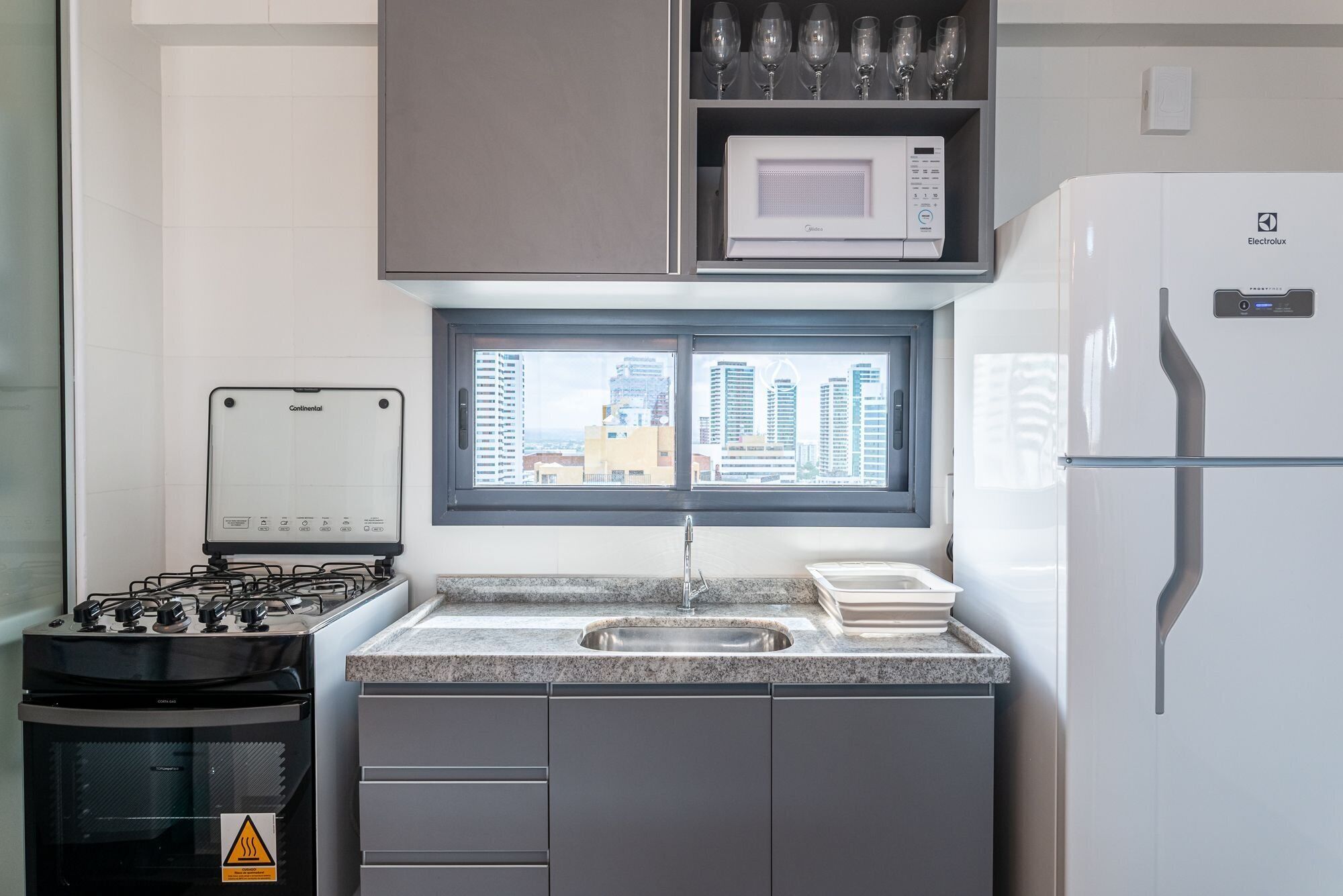 A compact kitchen with a gas stove, microwave, and refrigerator, a window with a city view, and a sink with a granite countertop.