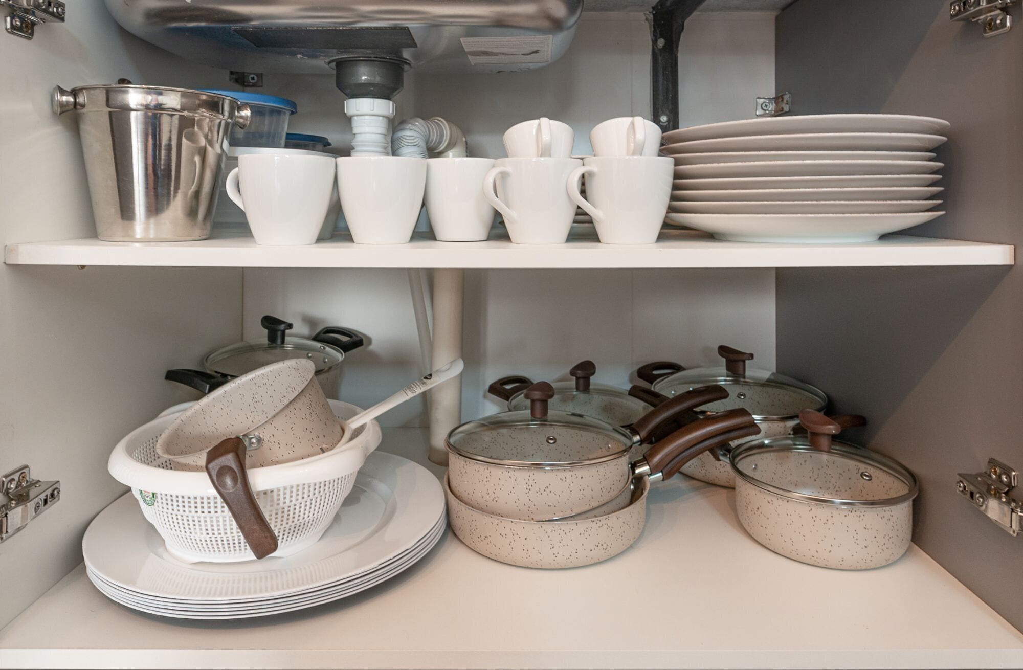 Una cucina con mensole bianche che contengono tazze, piatti e una colapasta, tutti bianchi.