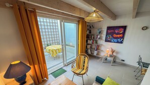 En stue med sofa, et bord, en lampe, bogreol og udsigt ud.