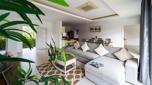 A modern living room with a grey sofa, a coffee table, and a dining area in the background. - Pool Villa Black Mountain Hua Hin BM30 (Hua Hin)