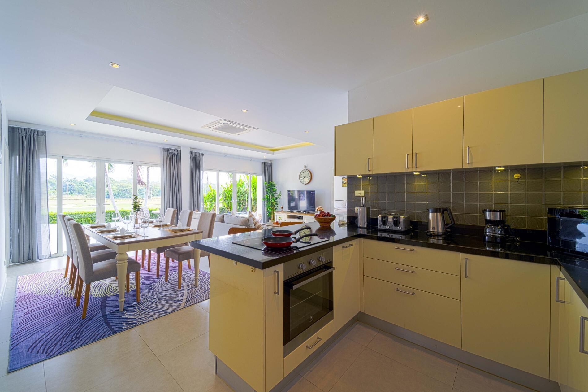 A modern kitchen with a central island, built-in oven, and a dining area with a table and chairs.