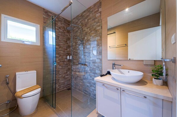 Une salle de bain moderne avec une douche à parois de verre, des toilettes blanches et un grand lavabo avec un miroir au-dessus.