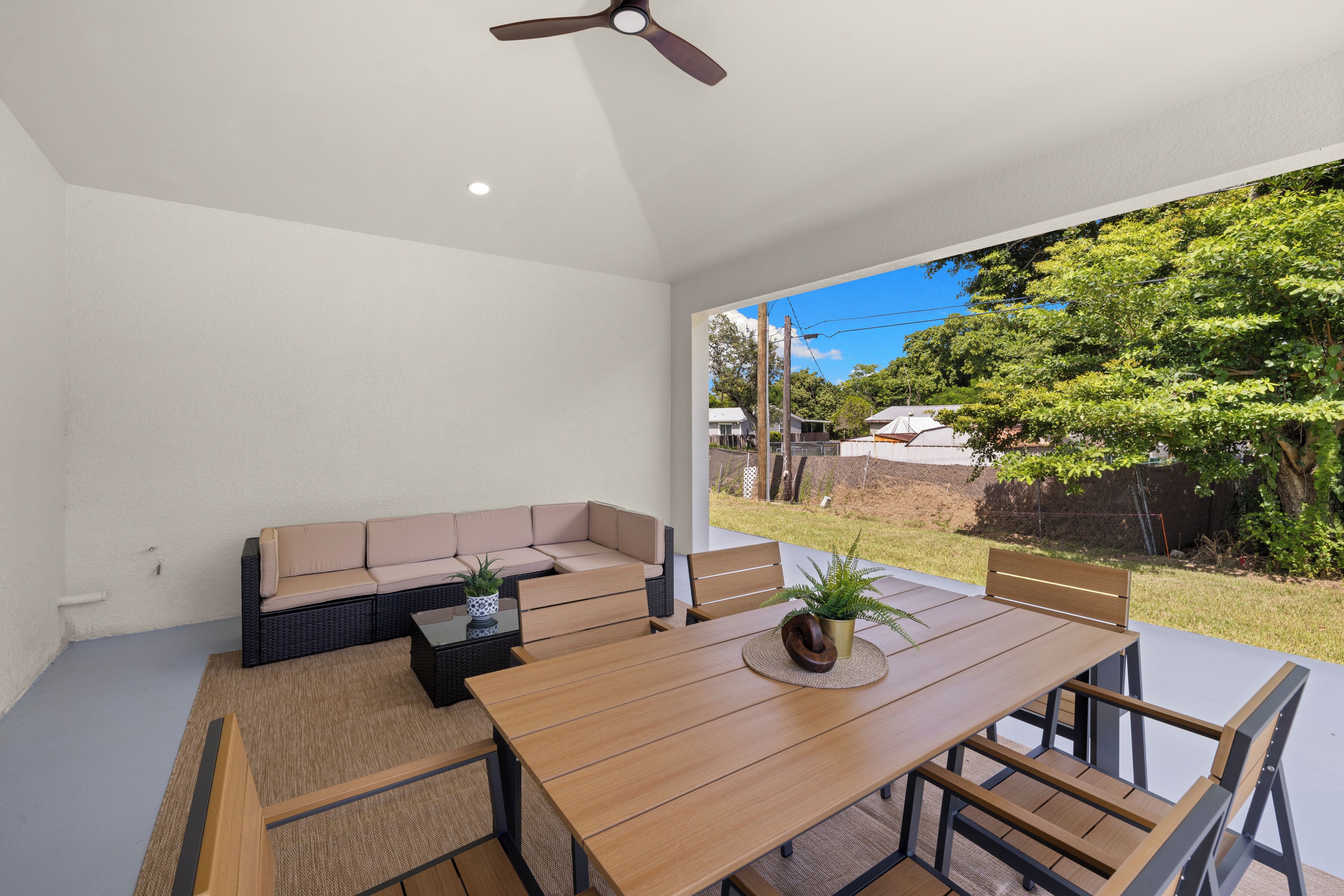 A modern outdoor patio with a wooden table and chairs, a beige sofa, and a ceiling fan.