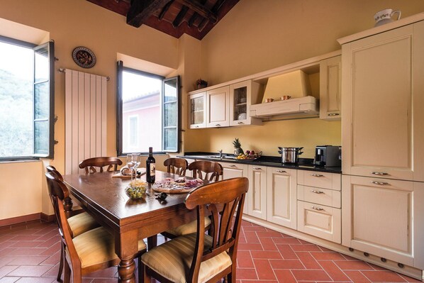 Een eethoek met een houten tafel, stoelen en een raam met open luiken.