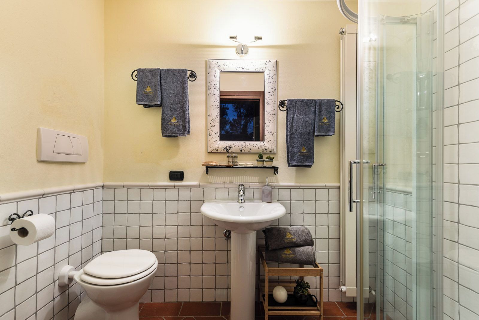 A bathroom with a toilet, sink, and shower. There are towels hanging on hooks and a mirror above the sink.