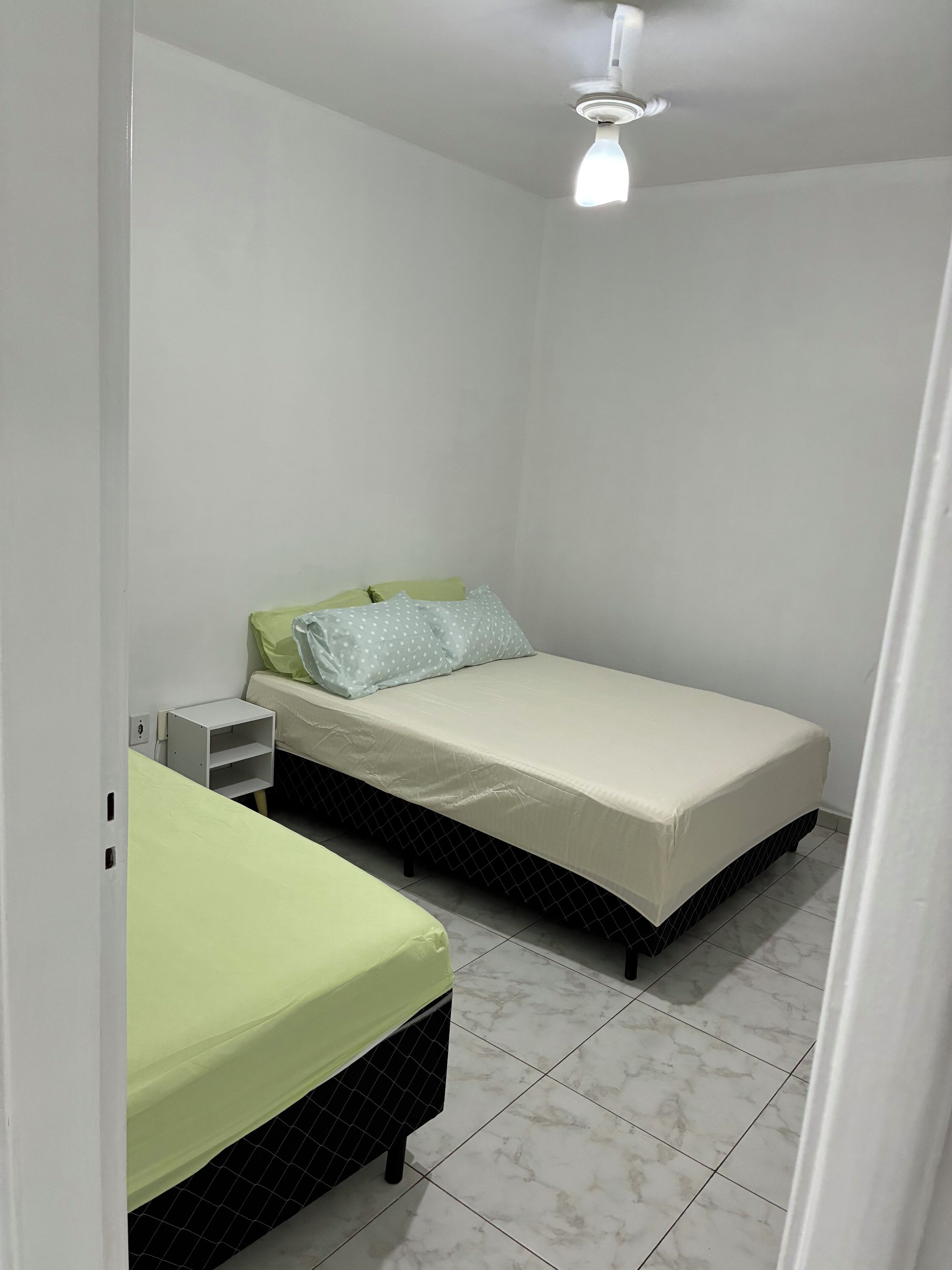 A small, clean room with a single bed, a nightstand, and a ceiling fan.