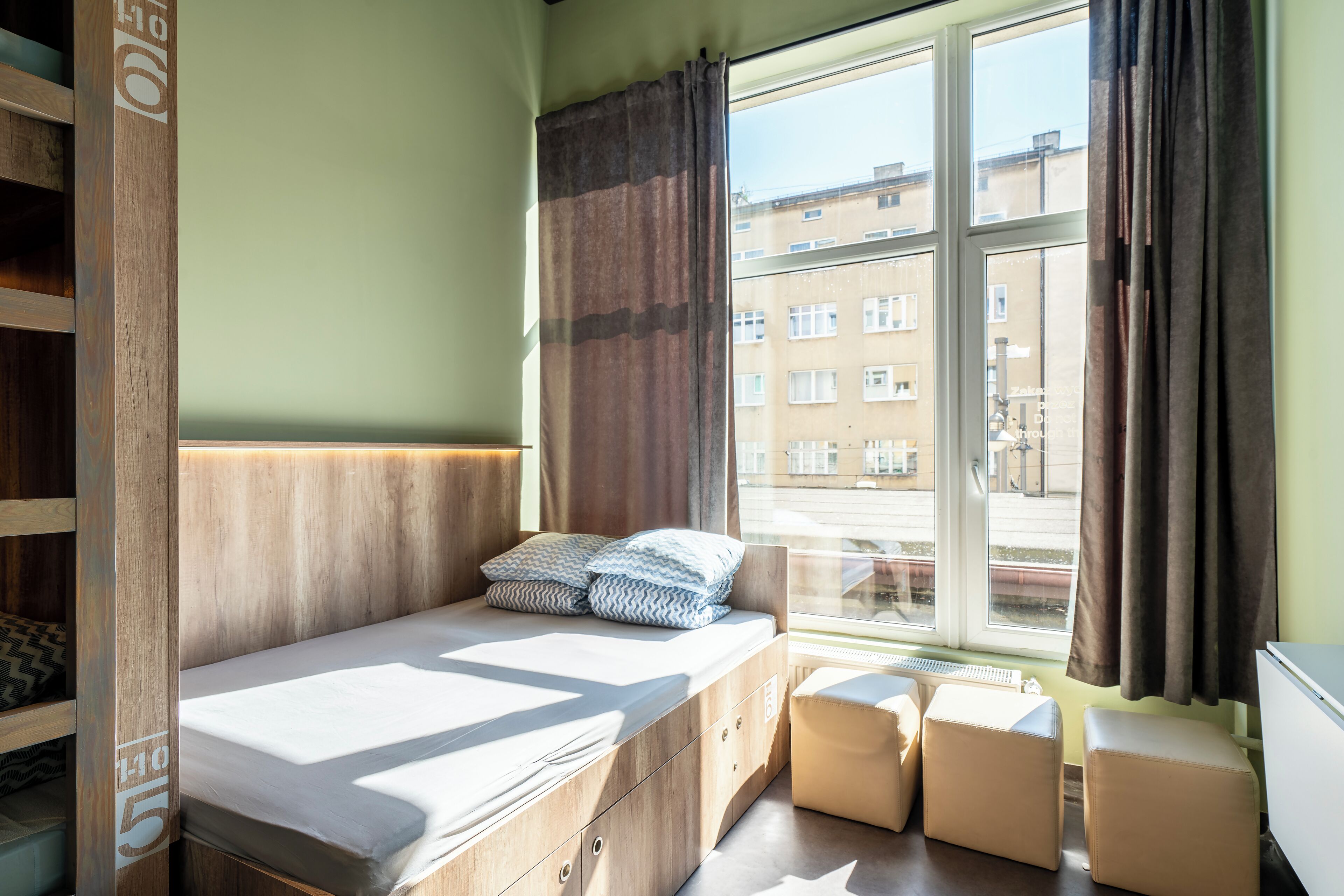 A room with a bed, a window, and a view of buildings outside.
