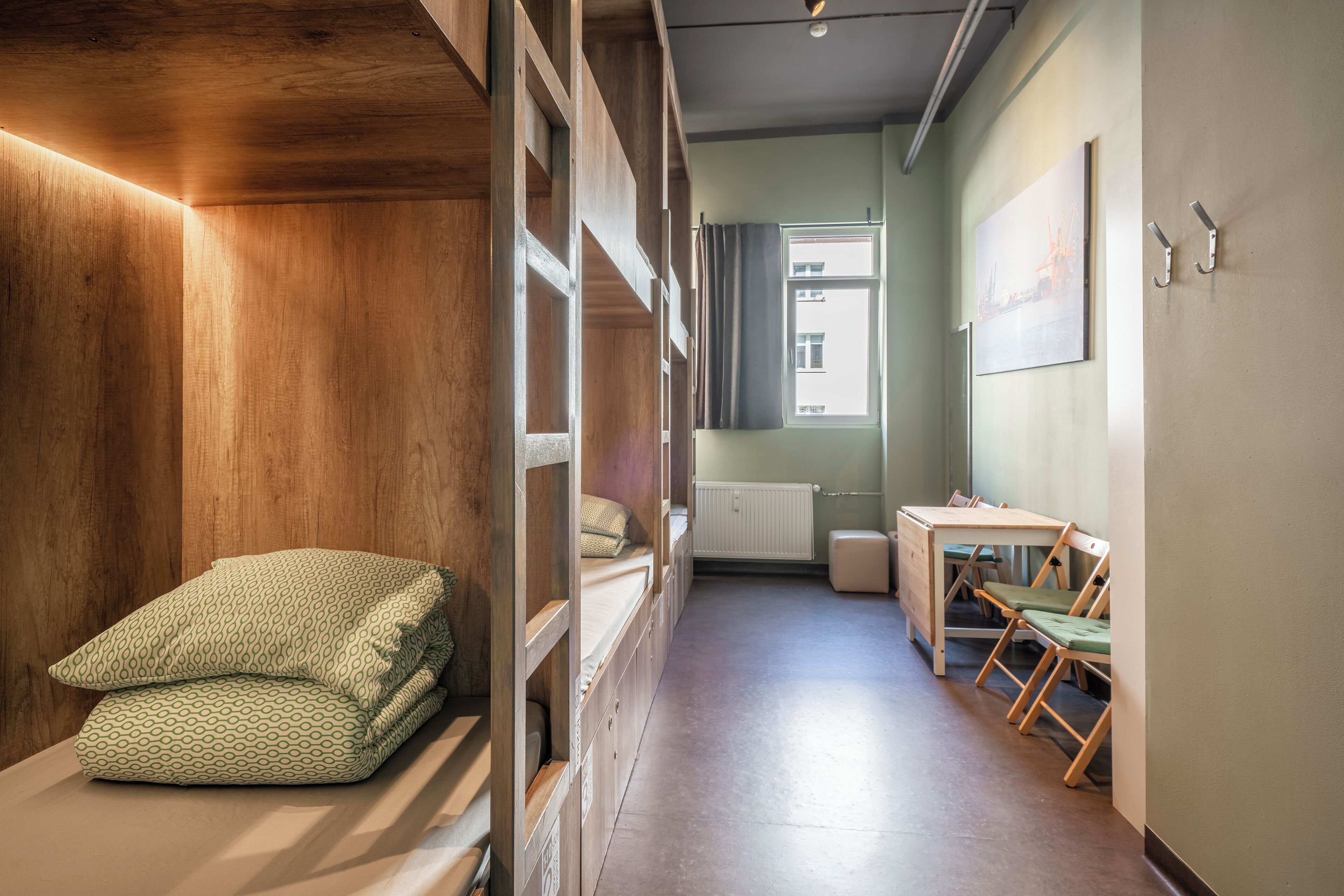 A room with bunk beds, a desk, and chairs, a radiator, and a window with curtains.