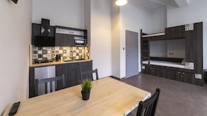 A compact kitchen with a microwave, stove, and sink, a dining table with chairs, and a bunk bed with a ladder. - 110 hostel (Gdynia)