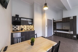Una cucina compatta con forno a microonde, fornelli e lavandino, un tavolo da pranzo con sedie e un letto a castello con scaletta.