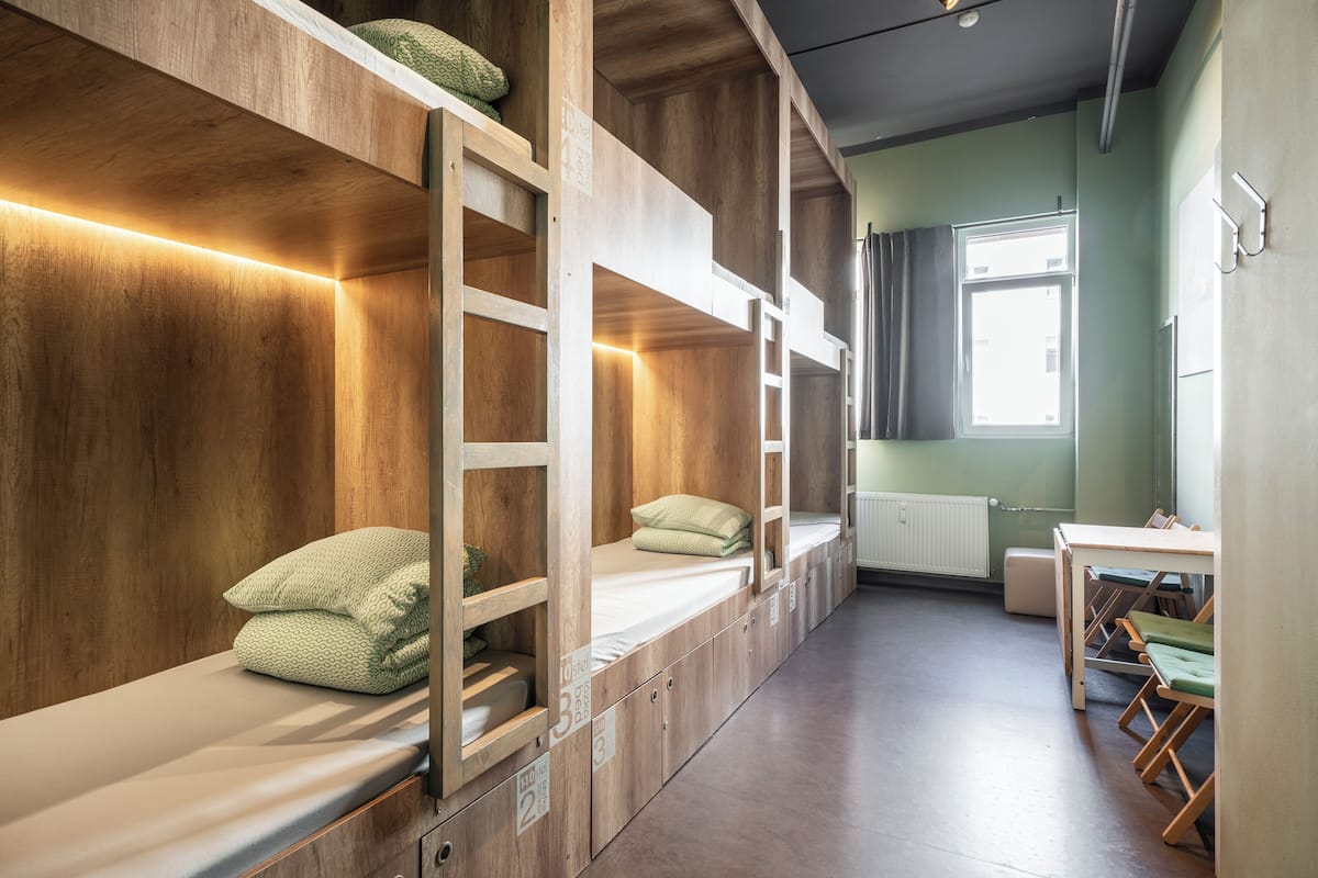 A bunk room with wooden bunk beds, a table, chairs, and a window.