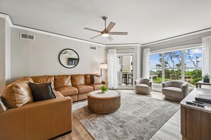A modern living room with a brown leather sofa, a round coffee table, and a ceiling fan. - Chic 1st Floor Villa w/ Balcony, Views & Amenities (Hilton Head Island)