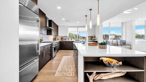 Una cocina moderna con electrodomésticos de acero inoxidable, una isla grande, iluminación colgante y vistas al exterior.